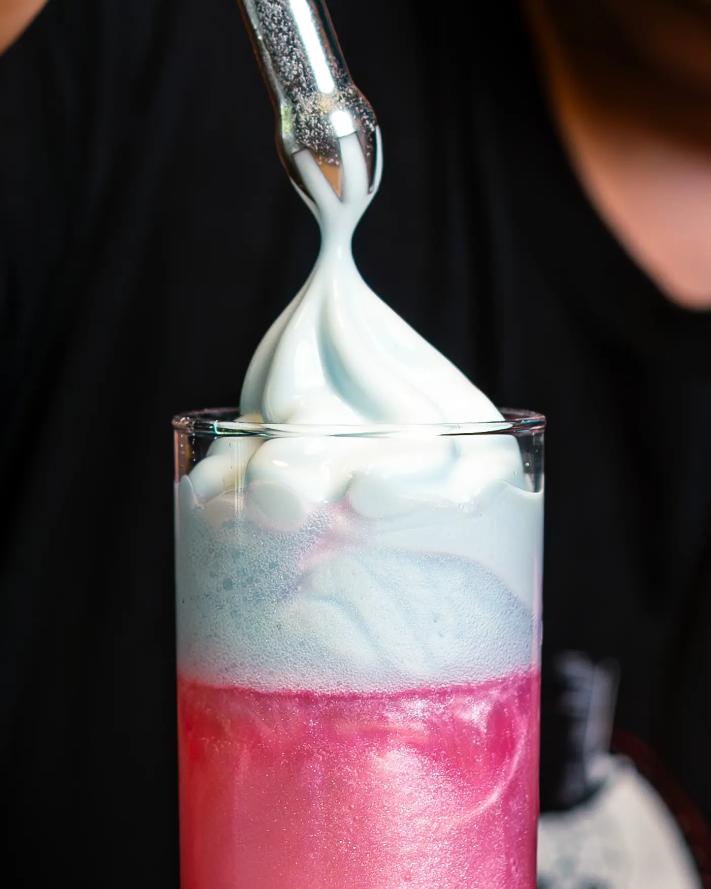 Spuma bianca versata su un cocktail rosa