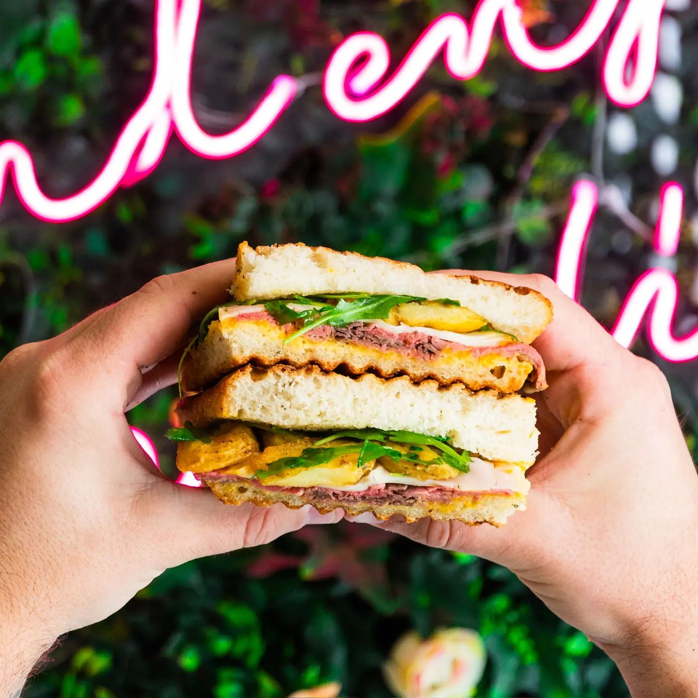 Panino farcito tenuto con due mani davanti a un'insegna al neon